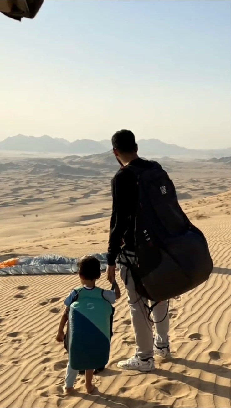 طيار وطفل يتجهان نحو مظلة الطيران وسط الكثبان